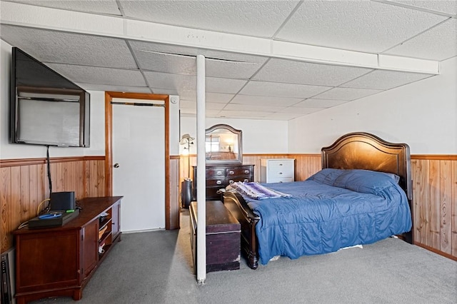 carpeted bedroom featuring wooden walls, a paneled ceiling, and a wainscoted wall