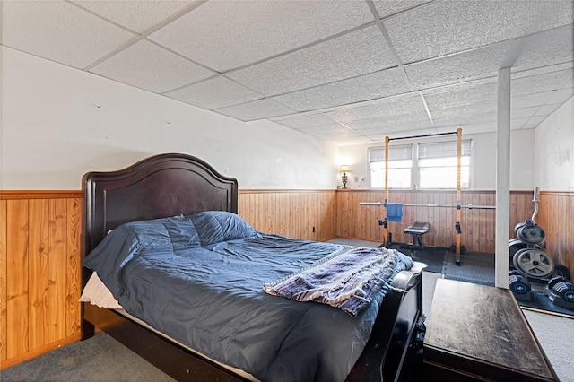 bedroom featuring a drop ceiling, a wainscoted wall, and wood walls