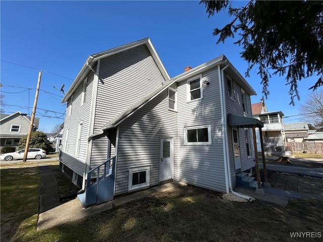 back of house with entry steps, fence, and a chimney