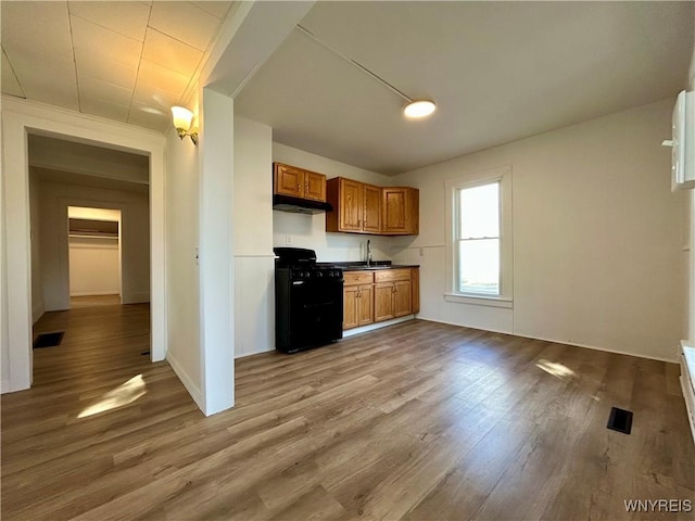 kitchen featuring visible vents, light wood finished floors, black gas range, under cabinet range hood, and brown cabinets