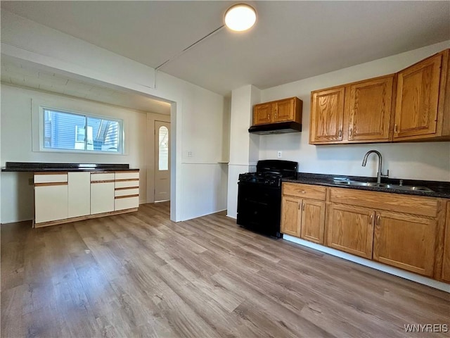 kitchen with a sink, black gas range oven, under cabinet range hood, and light wood finished floors