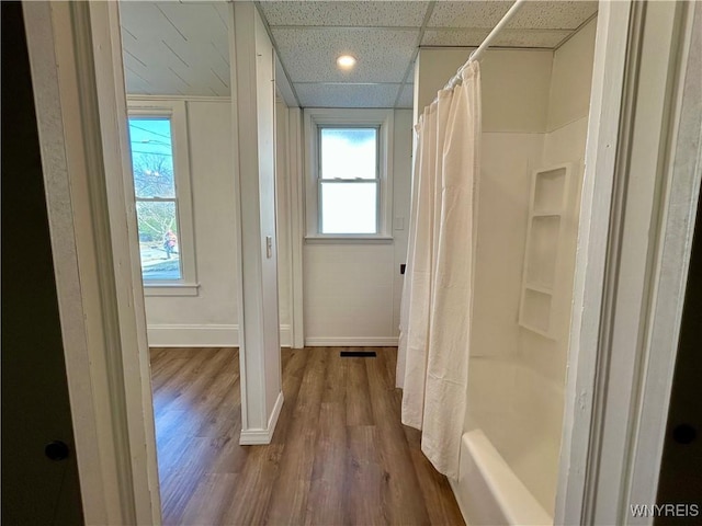 bathroom featuring a drop ceiling, baseboards, shower / tub combo with curtain, and wood finished floors