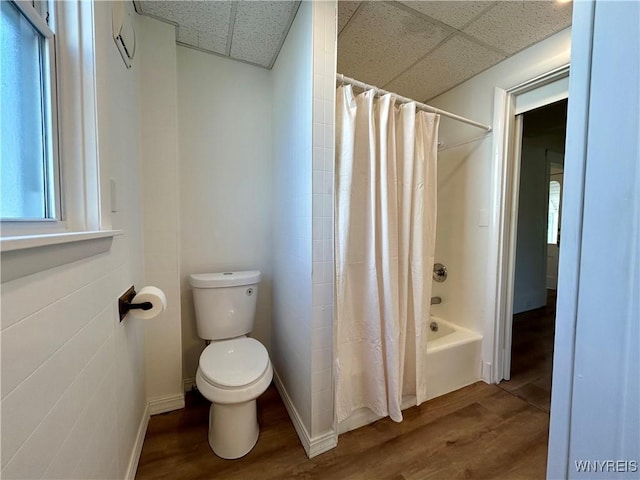 full bath featuring toilet, shower / bath combo, a drop ceiling, wood finished floors, and baseboards