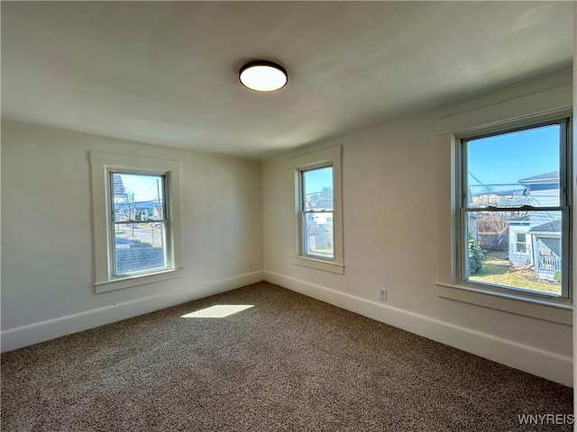 unfurnished room with a healthy amount of sunlight, dark colored carpet, and baseboards