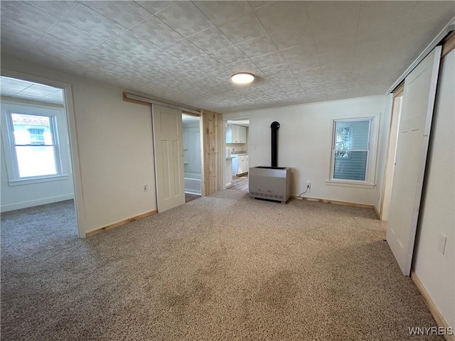 unfurnished bedroom featuring heating unit, baseboards, a wood stove, and carpet