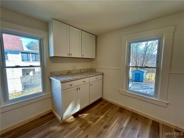 kitchen with white cabinets, plenty of natural light, wood finished floors, and wainscoting