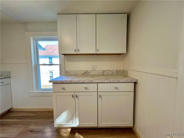 kitchen featuring wood finished floors, wainscoting, and white cabinetry