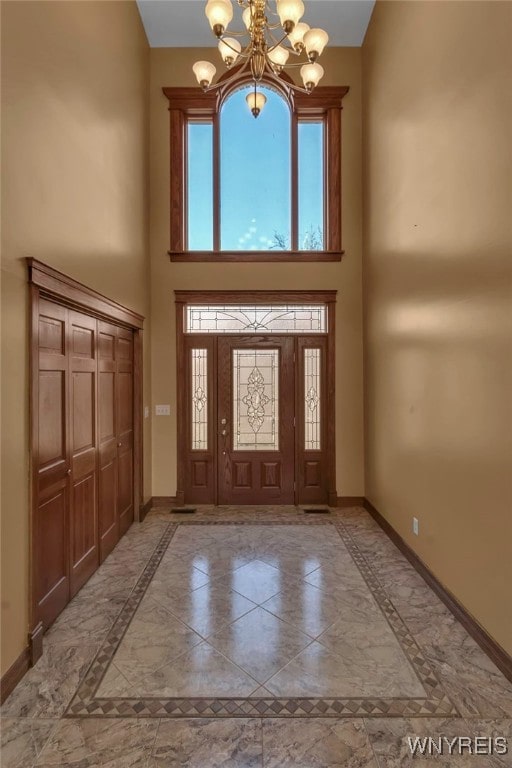 foyer featuring a healthy amount of sunlight, baseboards, a towering ceiling, and a chandelier