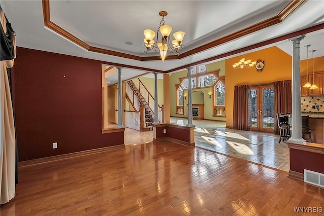 interior space with ornate columns, visible vents, a tray ceiling, and wood finished floors