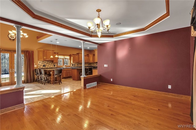 interior space with visible vents, a chandelier, a tray ceiling, light wood-style flooring, and ornate columns