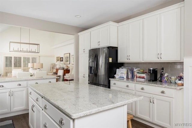 kitchen featuring light stone counters, a kitchen island, decorative backsplash, white cabinets, and black fridge with ice dispenser