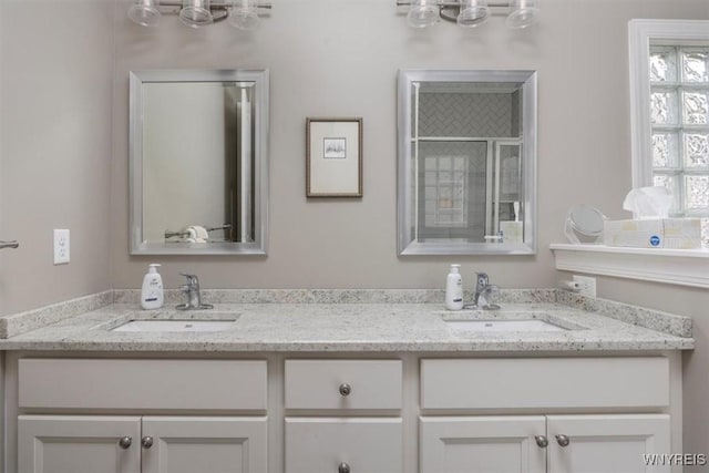 full bathroom featuring double vanity, a shower with shower door, and a sink