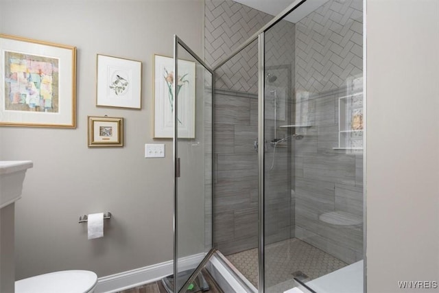 bathroom featuring a stall shower, toilet, and baseboards