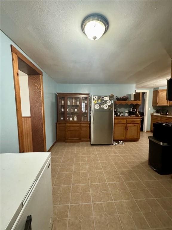 kitchen featuring brown cabinets, a textured ceiling, refrigerator, and freestanding refrigerator