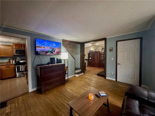 living room featuring baseboards, ceiling fan, stairway, ornamental molding, and hardwood / wood-style flooring