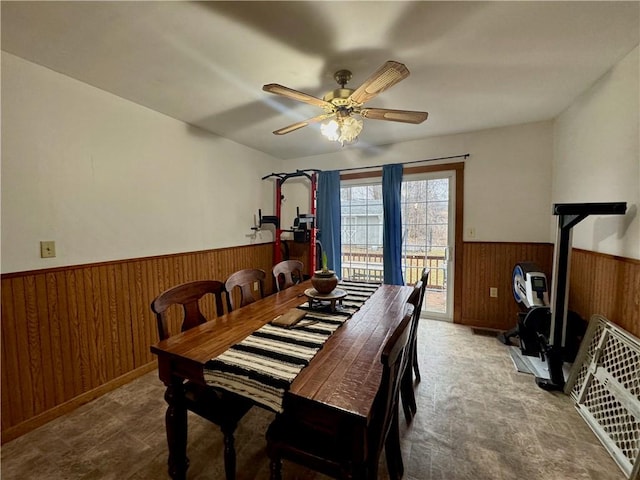 dining space with a ceiling fan, wood walls, and wainscoting