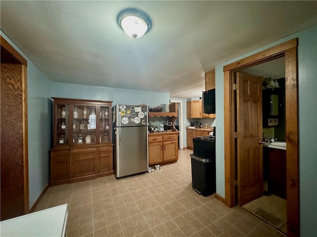 kitchen featuring freestanding refrigerator, brown cabinetry, light countertops, baseboards, and light floors