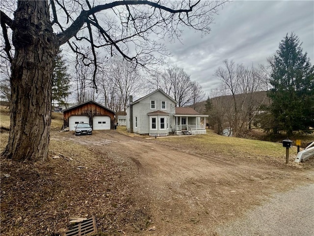 view of front of home featuring a detached garage, dirt driveway, a front yard, covered porch, and an outdoor structure