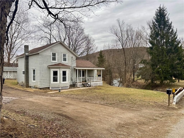 view of front of house with a front lawn, covered porch, roof with shingles, and a chimney