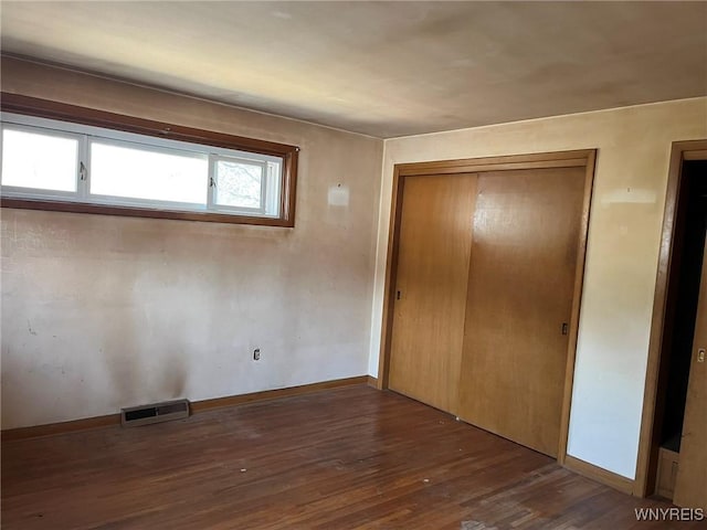 unfurnished bedroom featuring wood finished floors, visible vents, a closet, and baseboards