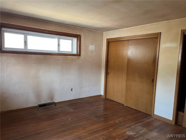 unfurnished bedroom featuring a closet, visible vents, baseboards, and wood finished floors