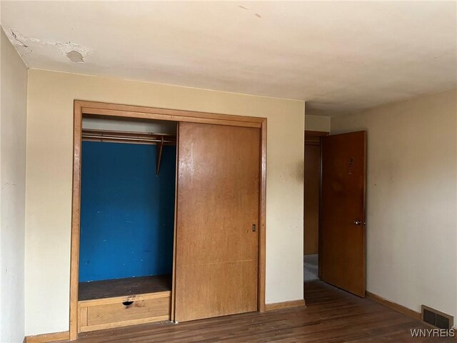 unfurnished bedroom featuring a closet, visible vents, baseboards, and wood finished floors