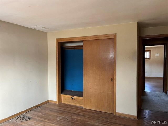 unfurnished bedroom featuring wood finished floors, baseboards, and a closet