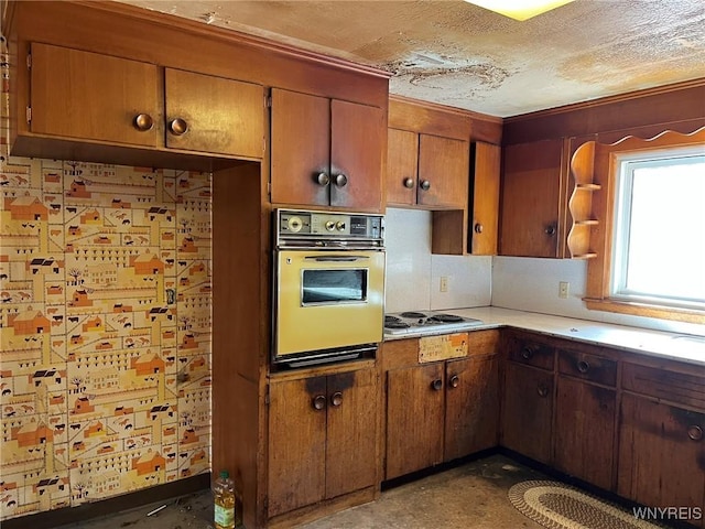 kitchen featuring white electric stovetop, oven, light countertops, a textured ceiling, and brown cabinets