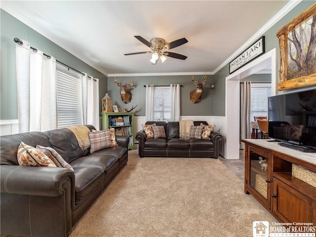 living room with a wainscoted wall, light colored carpet, ceiling fan, and ornamental molding