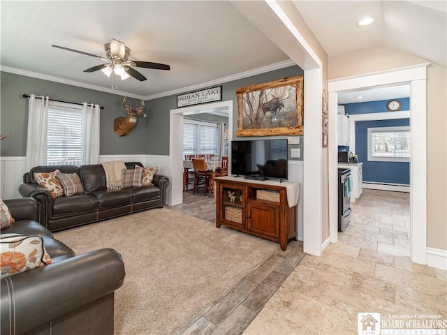 living area with ceiling fan, vaulted ceiling, ornamental molding, baseboard heating, and wainscoting