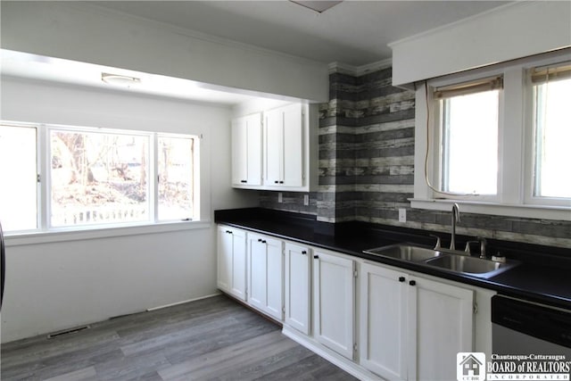 kitchen with dark countertops, white cabinets, dishwasher, and a sink