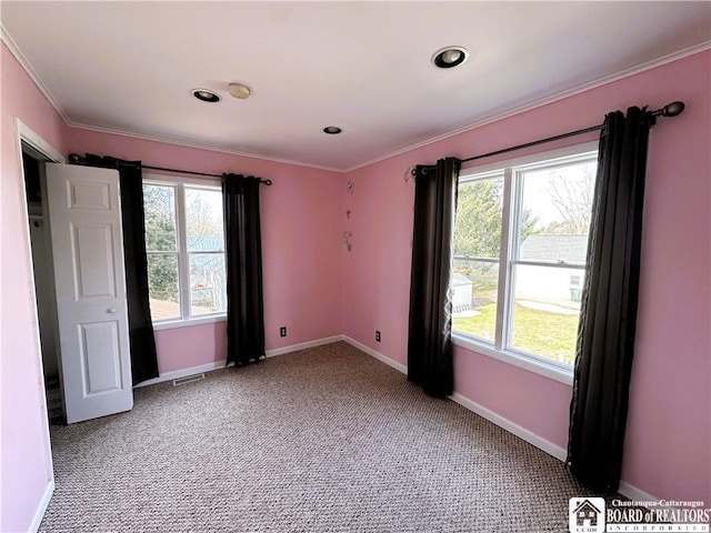 spare room featuring a wealth of natural light, baseboards, crown molding, and carpet