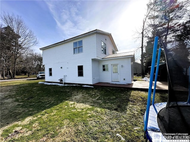 rear view of property with a deck, a lawn, metal roof, and a trampoline