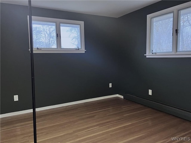 unfurnished room with baseboards, baseboard heating, and wood finished floors