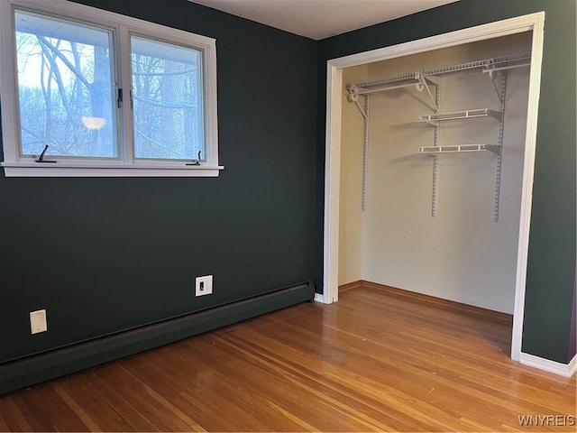 unfurnished bedroom with a closet, wood finished floors, baseboards, and a baseboard radiator