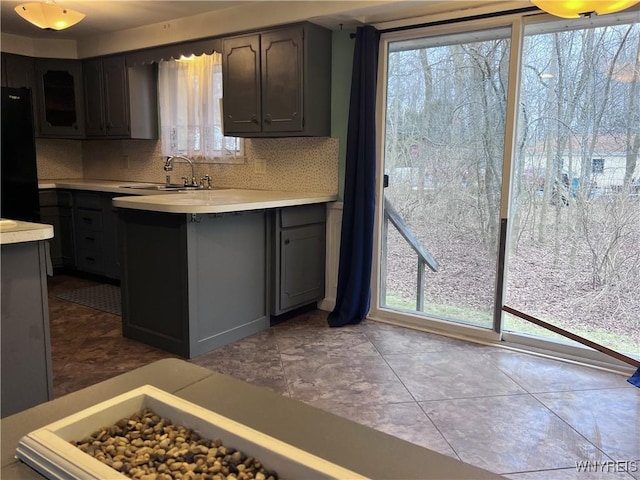 kitchen with a sink, backsplash, freestanding refrigerator, a peninsula, and light countertops