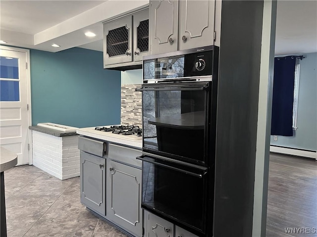 kitchen featuring backsplash, gray cabinetry, glass insert cabinets, baseboard heating, and dobule oven black