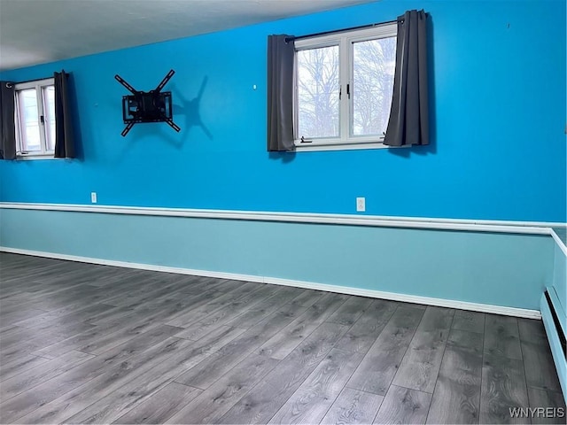 empty room featuring a baseboard radiator, baseboards, and wood finished floors