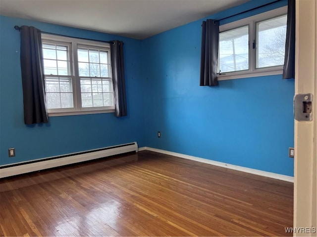 unfurnished room featuring a baseboard heating unit, baseboards, and wood finished floors