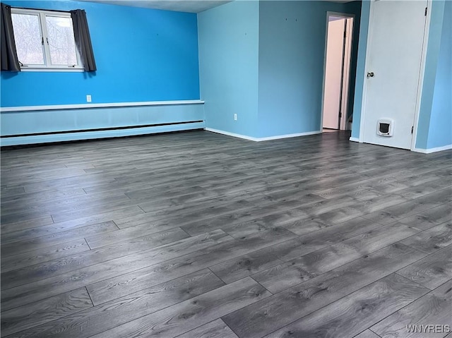 spare room featuring dark wood-style floors, a baseboard heating unit, and baseboards