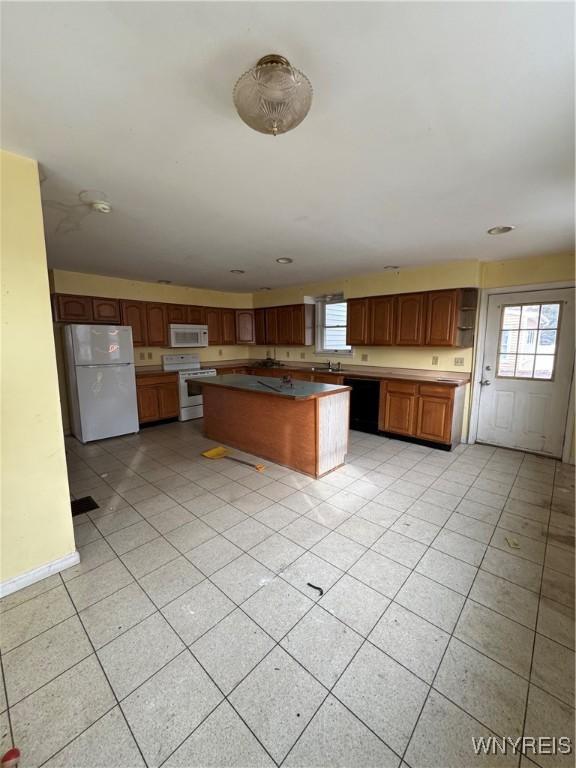 kitchen with light tile patterned floors, white appliances, a kitchen island, and plenty of natural light