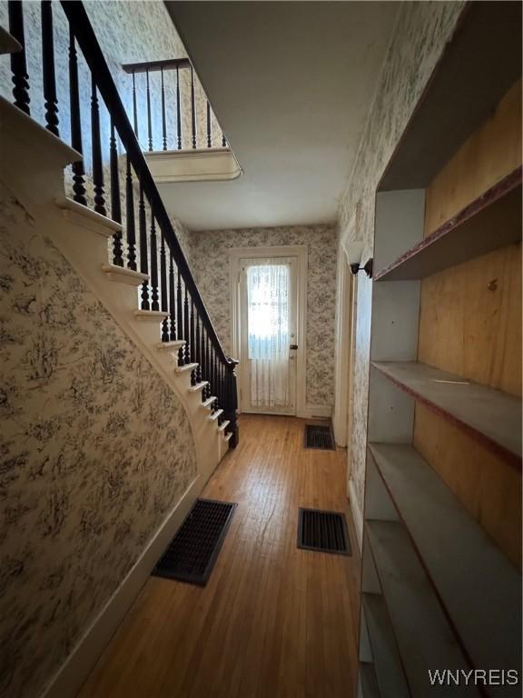 entryway featuring wallpapered walls, stairway, wood finished floors, and visible vents