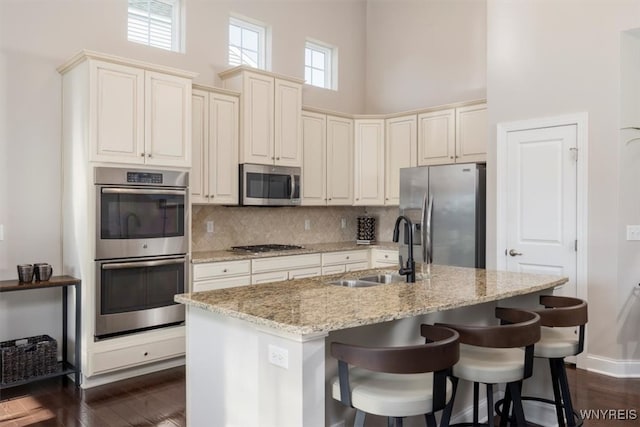 kitchen featuring a sink, a high ceiling, appliances with stainless steel finishes, decorative backsplash, and light stone countertops