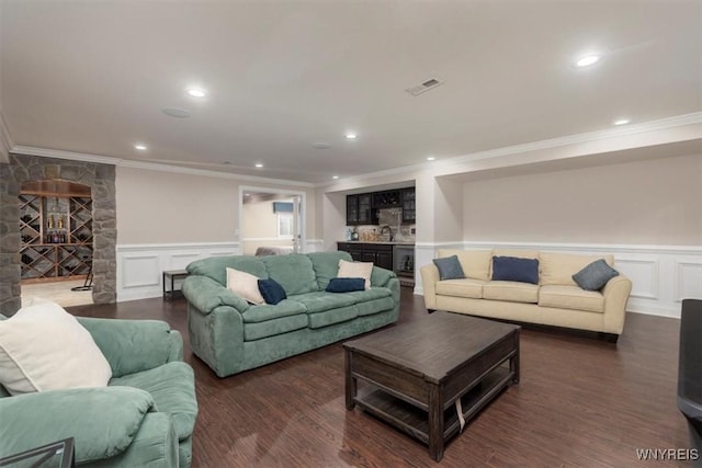 living area featuring a wainscoted wall, bar, ornamental molding, and wood finished floors