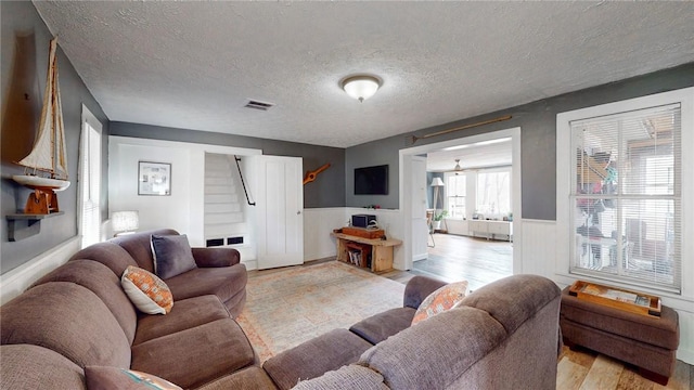 living area with a textured ceiling, visible vents, stairs, light wood finished floors, and wainscoting