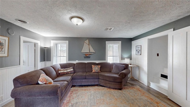 living room featuring wood finished floors, visible vents, a wealth of natural light, and a textured ceiling