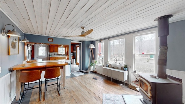 14838 W Lake Rd, Pulteney, NY 14418 - dining room with a wood stove, wooden ceiling, wainscoting, ceiling fan, and light wood-style floors