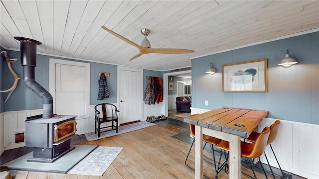 dining space featuring hardwood / wood-style floors, a wainscoted wall, a wood stove, ceiling fan, and wood ceiling