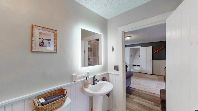 bathroom featuring a wainscoted wall, a sink, a textured ceiling, and wood finished floors