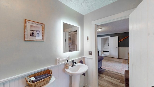 bathroom featuring a wainscoted wall, a textured ceiling, a sink, and wood finished floors